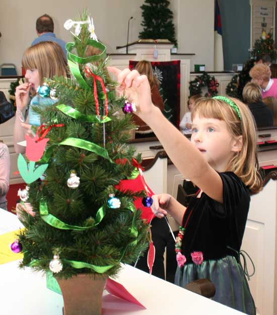 Deidra Kennedy reaches for an ornament on the “Blooms Year Round” tree at the Congregational Church.
