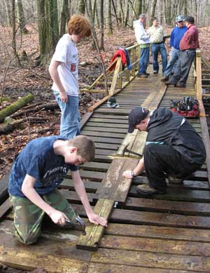 Eagle Scout candidate Nick Ostertag (foreground) puts the finishing touches on a new bridge, with help from Evan Cochrane, standing, and Tom Cooke. In the background, from left to right, Mark Beirbower, Bob Huber, Paul Willard, and Tony Shaw make use of the new structure. (Photo by Laura Andrews) Eagle Scout candidate Nick Ostertag (foreground) puts the finishing touches on a new bridge, with help from Evan Cochrane, standing, and Tom Cooke. In the background, from left to right, Mark Beirbower, Bob Huber, Paul Willard, and Tony Shaw make use of the new structure. (Photo by Laura Andrews)