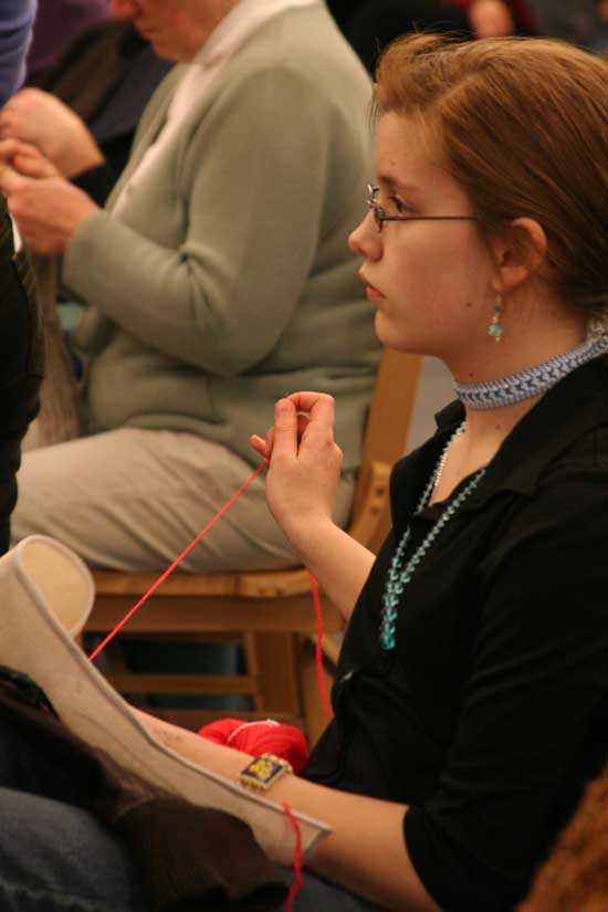 Becca Turner works on her needlepoint as she listens at the candidates debate.