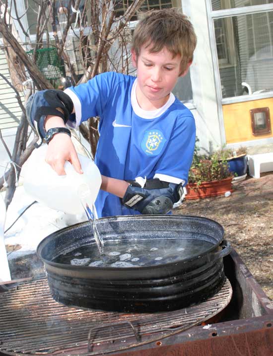 Eli Wood pours sap into a pan on an outdoor stove set up for sap boiling. Eli Wood pours sap into a pan on an outdoor stove set up for sap boiling.
