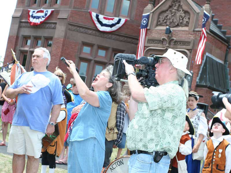Hat in hand, Ed Carter listens to Kathy Brule sing the national anthem as cameraman Boyd Estes captures the scene for a PBS documentary on American composer Charles Ives and his holiday symphony.