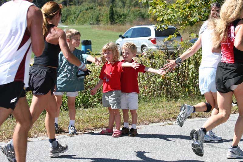 Christopher, Ariana, and Nicholas Thornton give high fives of encouragement to runners at the 8½-mile mark of the Apple Harvard Ramble road race in Harvard on Sunday. More than 800 runners participated.