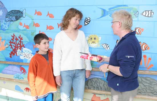 Alicia Dwyer receives a gift from Bess Haire of For Art's Sake for the fish mural she painted at the elementary school as her son Luke Karis looks on.