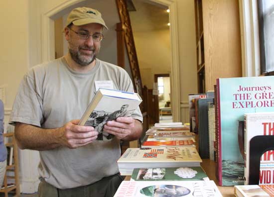 Friends of the Harvard Public Library President Chris Frechette takes a break from shelving to check out a book.