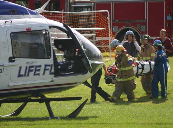 Harvard firefighters and paramedics transport an injured bicyclist who lost control on Oak Hill Road to a Lift Flight helicopter at the elementary school on Labor Day, Sept. 7. (Courtesy photo)