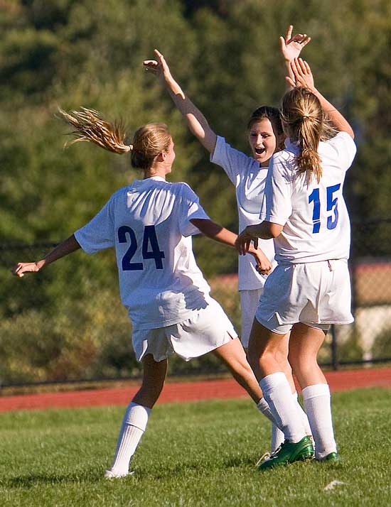 Susannah Wright (#24), Grace Bilodeau (center), and Katja Lierhaus (#15) celebrate after Bilodeau scores a goal against Littleton on Sept. 21. The Trojans beat the Littleton Tigers 4–0.