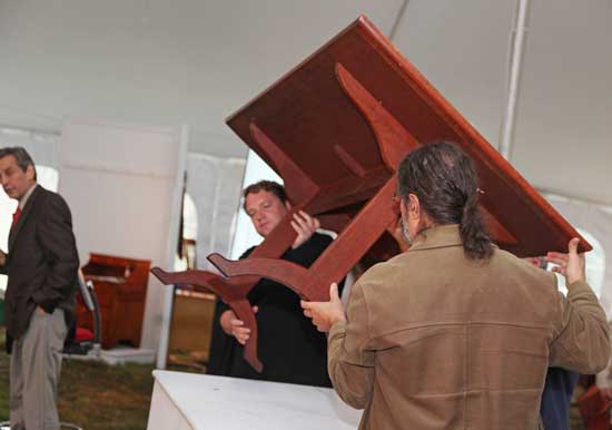 Auctioneer Willis Henry (far left) looks on as two of his helpers hoist a Shaker table onto a viewing podium. After several minutes of bidding, a bidder bought the the table­—one of only two its size to be held in private collections—for $100,000.