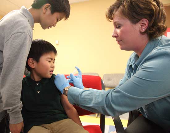 Kee Hwang Lee (left) looks over the shoulder of his little brother, Kee Seok, as Registered Nurse Tamara Bedard prepares to deliver an H1N1 vaccine at a clinic held at Bromfield in December.