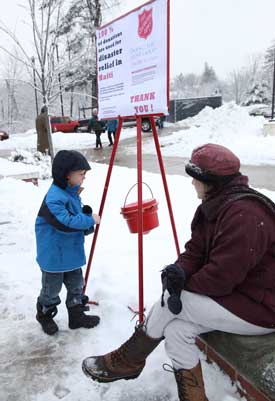 Four-year-old Austin Backer-Verbits puts his donation for Haiti relief into a Salvation Army bucket as volunteer Melissa Marteney looks on. (Photo by Lisa Aciukewicz)