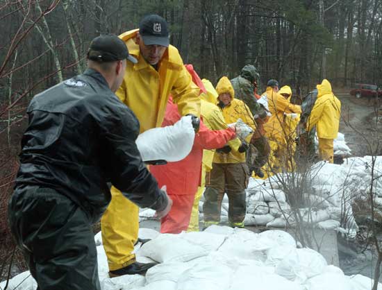 Members of the DPW and Fire Department form a bucket brigade as they pass sandbags to shore up the dam on Bare Hill Pond on March 30