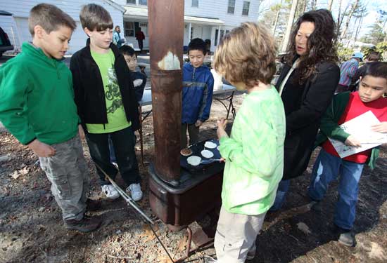 From left: Oliver Smelanskas, Baylor Ashe, Liam Wang, Kevin Yu, Jack Donaldson, Sara Bibbo, and Antonio Bibbo gather ‘round to watch the progess of the pancakes as they cook atop a woodstove griddle.