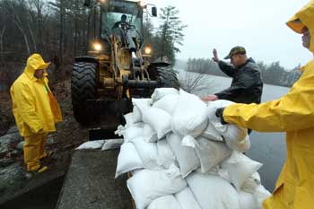 Firefighter Greg Harrod (center) gives the stop signal to a DPW loader operator delivering a pallet of sandbags to the dam on Bare Hill Pond. (Photo by Lisa Aciukewicz) Firefighter Greg Harrod (center) gives the stop signal to a DPW loader operator delivering a pallet of sandbags to the dam on Bare Hill Pond. (Photo by Lisa Aciukewicz)