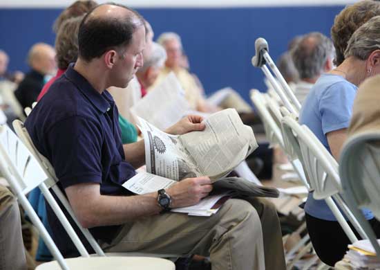 A town meeting attendee keeps informed with the Harvard Press.
