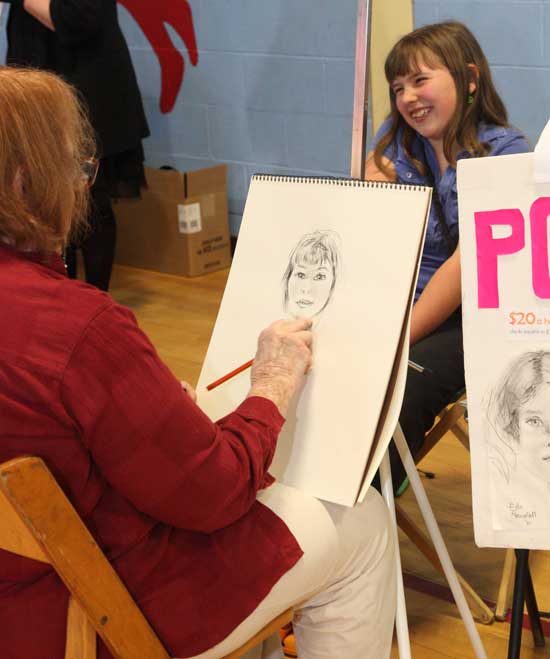 A sketch artist draws a portrait of fourth-grader Penelope Schnier at the Rotary Club Apple Blossom Festival on May 8, held inside at Hildreth Elementary School because of rain.