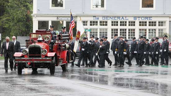 The Harvard Fire Department turns out in full force to bid a final farewell to long-time firefighter and lifelong Harvard resident Ken Harrod as it follows his casket around the Common on a very rainy May 8.