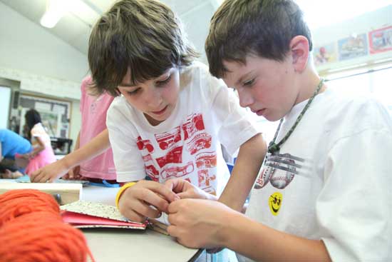 Hunter Carroll (left) helps Lance Jarosz sew his book together. 