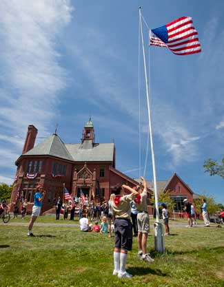 A Boy Scout salutes as another raises the flag in front of Old Bromfield on July 4. (Photo by Ellen Harasimowicz)