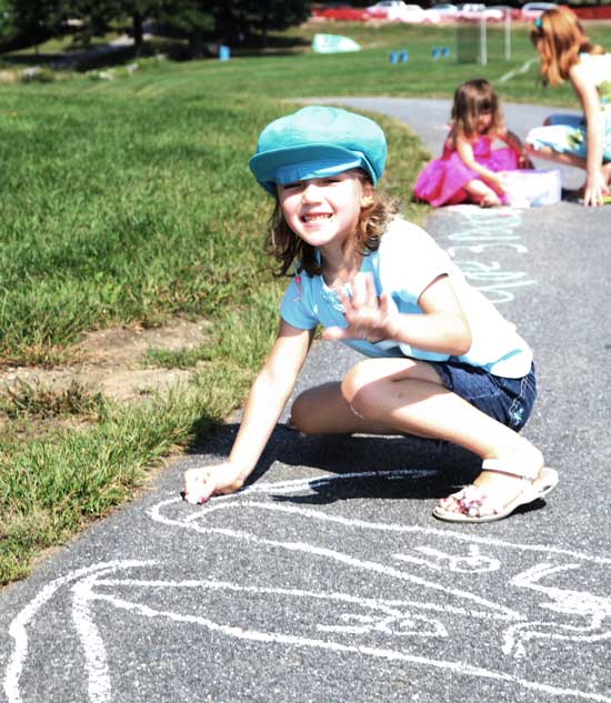 Chloe Palmer looks up from her chalk art at the kindergarten picnic in front of the library.