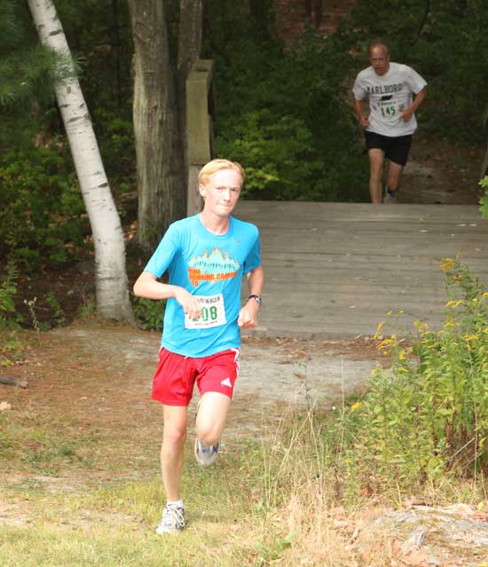 Ellis Toll runs out of the wooded section of the 5K race, with Matt Day following over the bridge. Toll took second overall in the race and took first place for Harvard entrants with a time of 18:44.