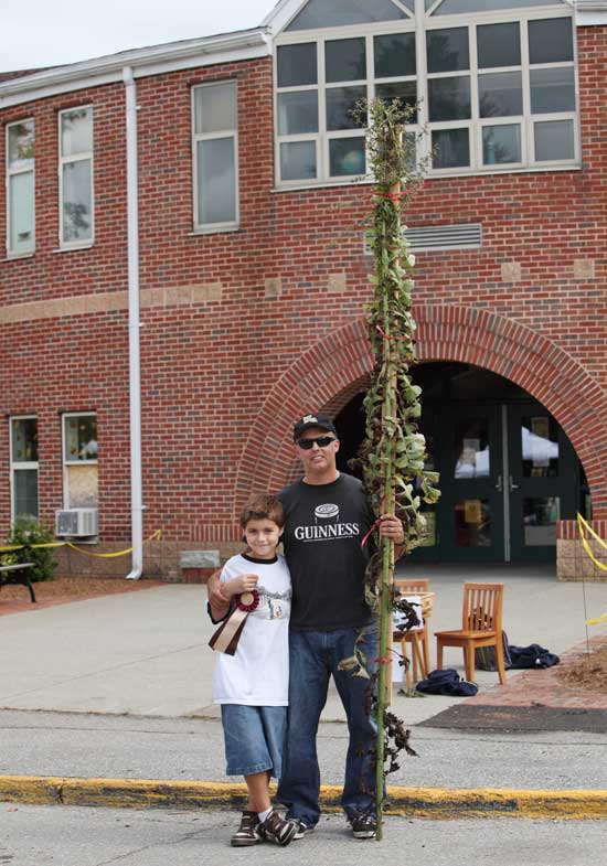 Christopher Bunnell (left) displays his first-place ribbon as his father, Patrick, holds up their prize-winning weed in front of the elementary school at a recent Farmers' Market..