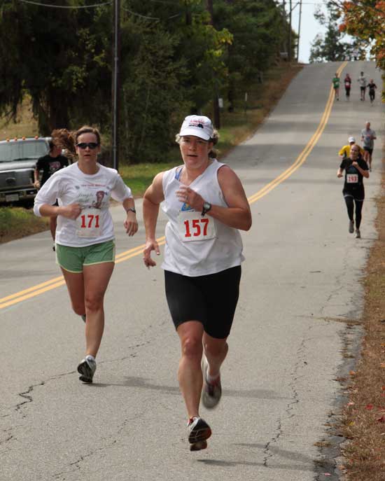 Beck Furniss of Brookline (left) and Alison Thornton of Harvard (right) lead a pack of runners down the hill toward the finish line at Fruitlands.