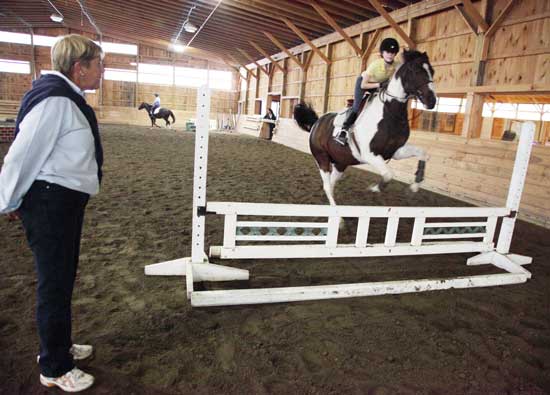 Patti Harnois (left), the new head trainer at Meadow March Riding Center, watches as Gabriella McCarthy clears a jump atop Flower, a Pinto horse.
