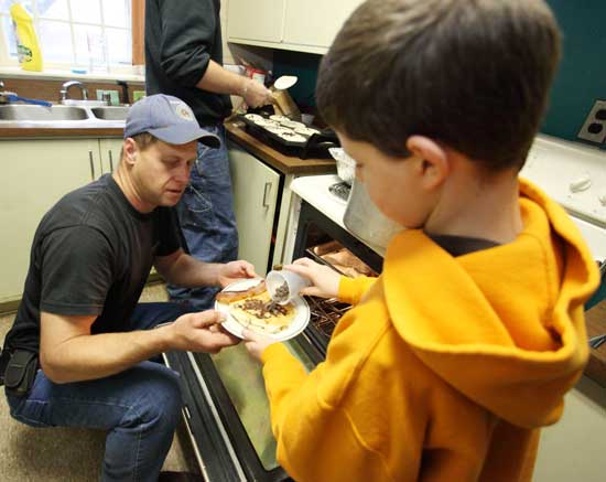 Greg Harrod puts bacon on a plate of pancakes, and his son Chris proceeds to add the secret ingredient—chocolate chips—at a breakfast at the fire station for the winners of the fire and life safety contest. 