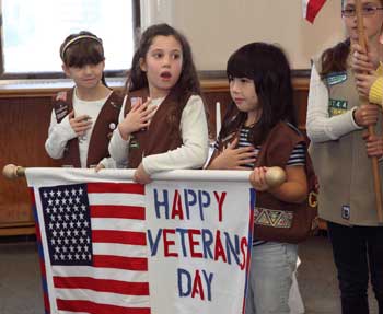 From left, elementary school students and brownies Bridget Kennedy, Marley Ferguson,  and Allie Hunter hold a banner as Katie Erdos holds a flag at a Veterans Day ceremony in the old library. (Photo by Lisa Aciukewicz)