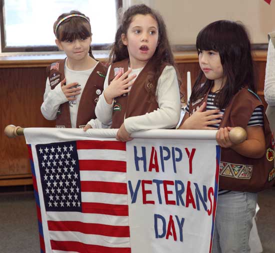 Brownie Scouts Bridget Kennedy, Marley Ferguson, and Allie Hunter hold a banner at a Veterans Day ceremony.