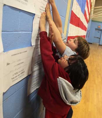 Max Chadran (left) and Jack Kelley put up the last “bricks” in a wall of papers honoring service members­—past and present—related to children at the elementary school. (Photo by Lisa Aciukewicz)