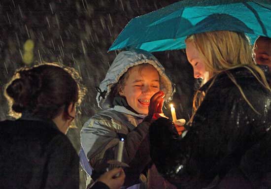 Liza Agosta gets help protecting her candle’s flame from Emma Sullivan and her umbrella.
