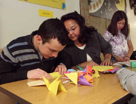 Philip Wesley (left) gets some coaching from Lois Krautz on his origami as Sylvia Ren (far right) works on her own project.