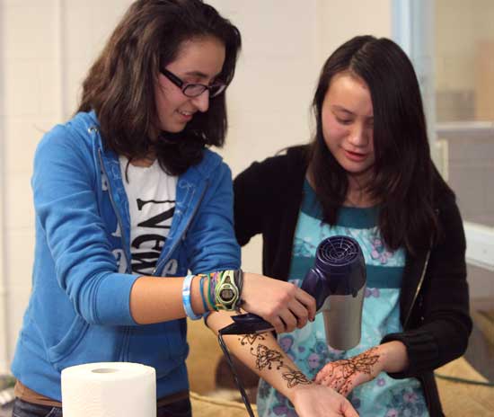 Nicole Into (left) and Tiffany Khuu dry the henna design on their hands and forearms with a hair dryer.