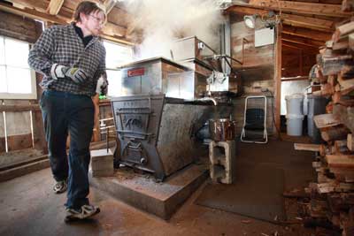 Constantly in motion, Jim Burns rounds the corner of his boiler to load more wood into the woodstove in his Ayer Road sugarhouse. (Photo by Lisa Aciukewicz)