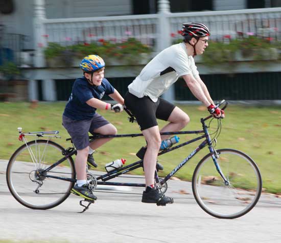 Tommy Nigzus (left) rides behind Doug Browne on a tandem bicycle.