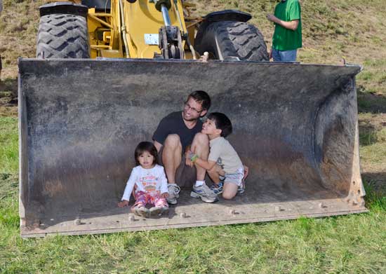 From left: Junyi Frenzel, Martin Frenzel, and Liam Frenzel check out the bucket of a front-bucket loader at the “touch a truck” demonstration. (Photo by John Sharko)