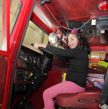 Cecilia takes the wheel of a parked fire truck. Cecilia takes the wheel of a parked fire truck.