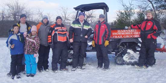 Members of the Harvard Snowmobile Club pose in front of their trail groomer at a cookout last winter. (Courtesy photo)