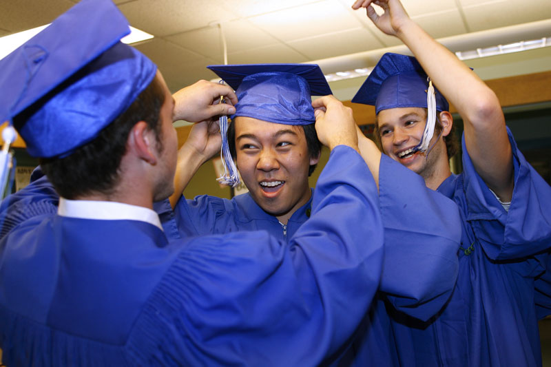 Charlie Watkins, left, and Chris Kenney, right, help Lanny Sun with his cap before the graduation ceremony. (Photo by Ellen Harasimowicz)