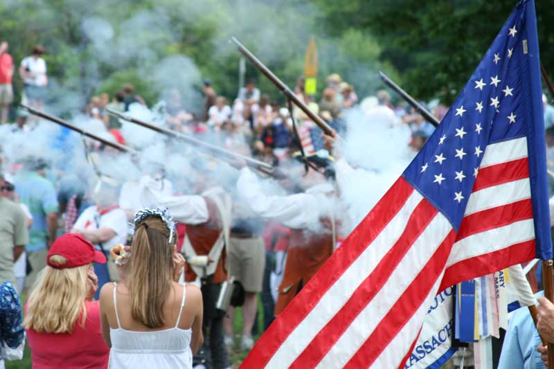 Spectators cover their ears as minutemen fire their muskets.