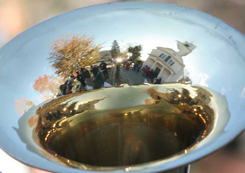The Nashoba Valley Band, as seen in the bell of a horn, plays carols in front of the church despite a bitter wind.