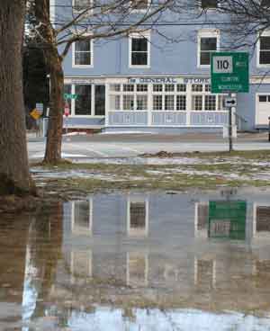 The General Store, as reflected in a puddle from this week’s drenching rain, is slated to re-open this spring. (Photo by Sue Fitterman)