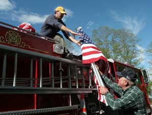 Bill Barton receives a flag from Warren Harrod as they load the fire truck to place flags on the Common. (Photo by Lisa Aciukewicz) 