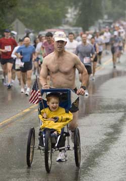 David Thieme, 5, of Devens, enjoys the ride as his father, US Marine Don Thieme, does all the work in the Great Harvard July 4th 5 Mile Road Race. (Photo by Ellen Harasimowicz)