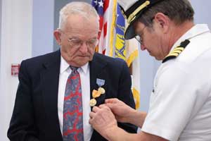 Roland Martineau watches as Selectman Ron Ricci pins medals on his suitcoat. Martineau received the American Campaign medal, Asiatic Pacific Theatre Campaign medal with one bronze star, World War II Victory medal, and Philippines Liberation medal with one bronze star. The medals reflected his service in the U.S. Navy during World War II when he served in the Pacific theatre of operations.