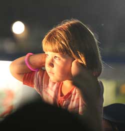 Sitting atop her father’s shoulders, Tally Dutkewych covers her ears during the concert.