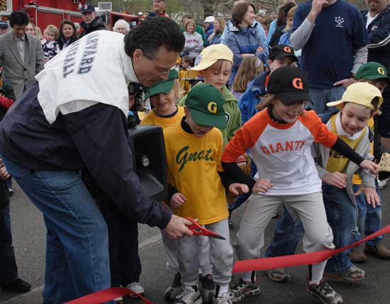 Dave Vellente cuts the ribbon on baseball’s opening day in April as players stand ready.