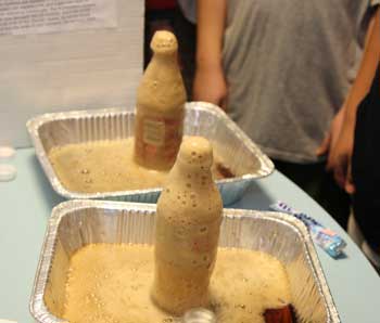 Coke foams and flows rapidly out of its bottle after a Mentos candy is dropped in.