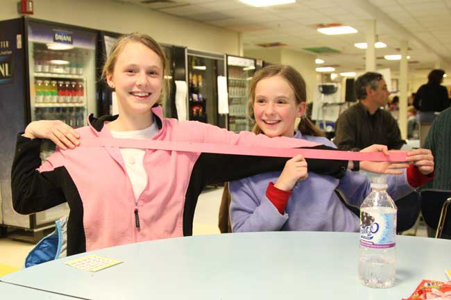 Kara Kennedy extends her arm as Deidre Kennedy measures the “arm’s length” of raffle tickets the pair bought.