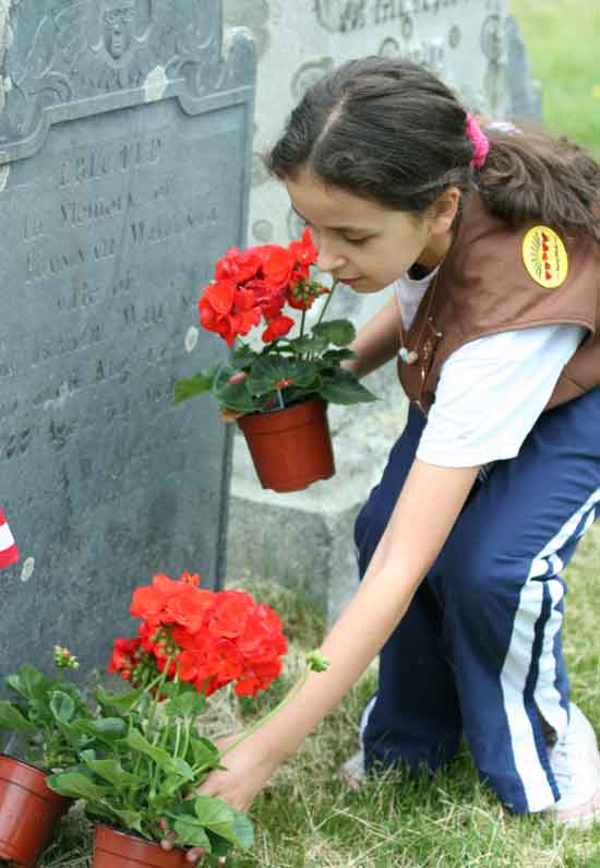 Girl Scout Nicole Into places geraniums on a veteran’s grave.
